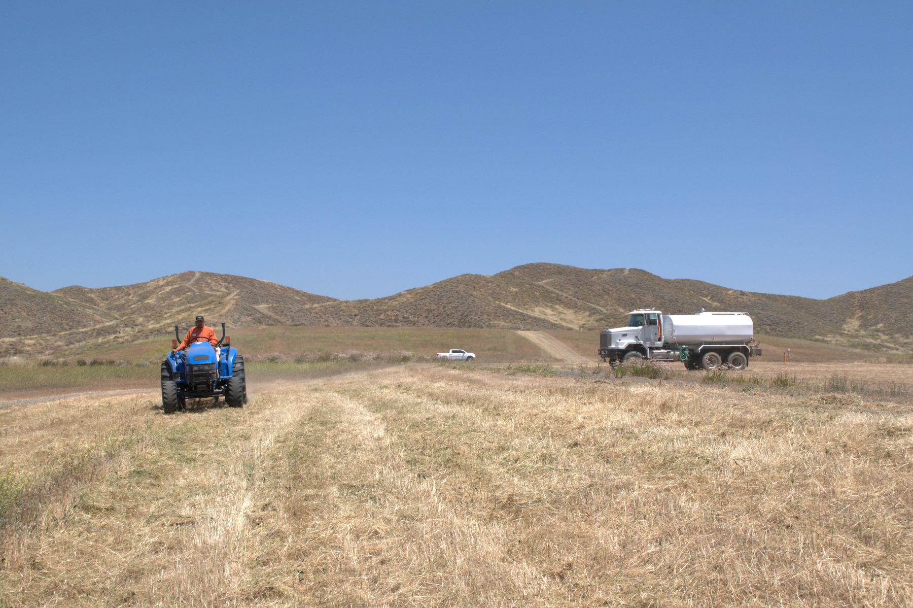 Operator mowing a large open property with a water truck nearby