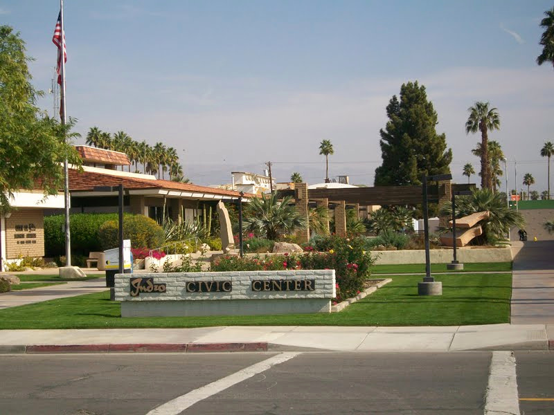 Municipal property frontage with lawn, shrubs, mature palms, and a monument sign